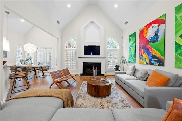 living room with wood finished floors, high vaulted ceiling, plenty of natural light, and a fireplace with raised hearth