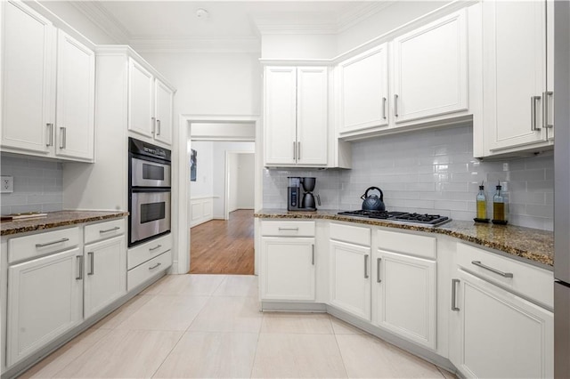 kitchen with appliances with stainless steel finishes, ornamental molding, dark stone counters, tasteful backsplash, and light tile patterned flooring