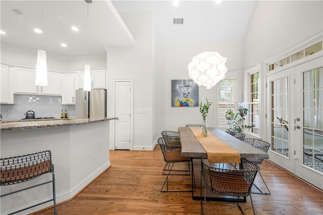 dining area with french doors, light wood finished floors, a high ceiling, baseboards, and a chandelier