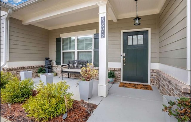 doorway to property featuring a porch and brick siding