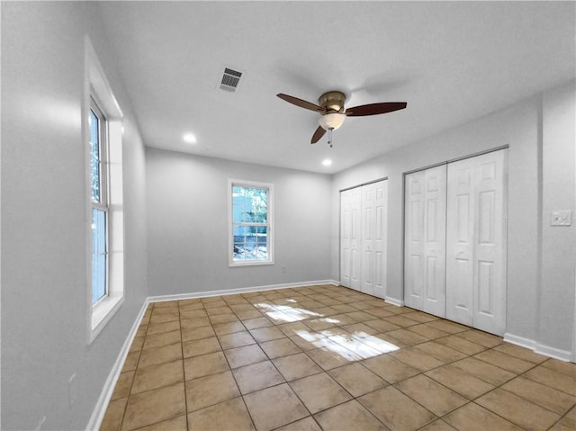 unfurnished bedroom featuring ceiling fan, multiple closets, and light tile patterned floors