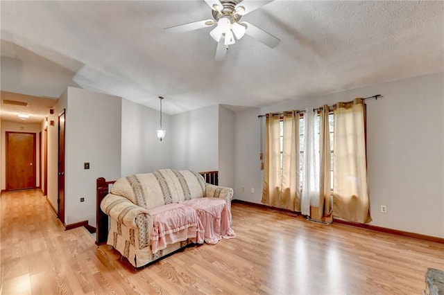 living room featuring light wood-type flooring, ceiling fan, and a textured ceiling