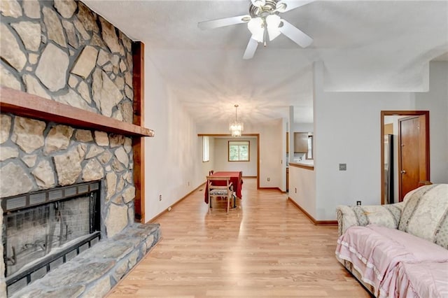 living room with ceiling fan with notable chandelier, a stone fireplace, and light hardwood / wood-style flooring