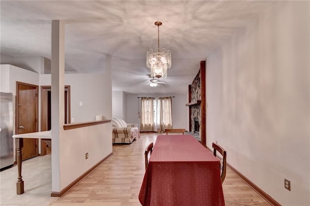 dining room with ceiling fan with notable chandelier, light hardwood / wood-style floors, and a fireplace