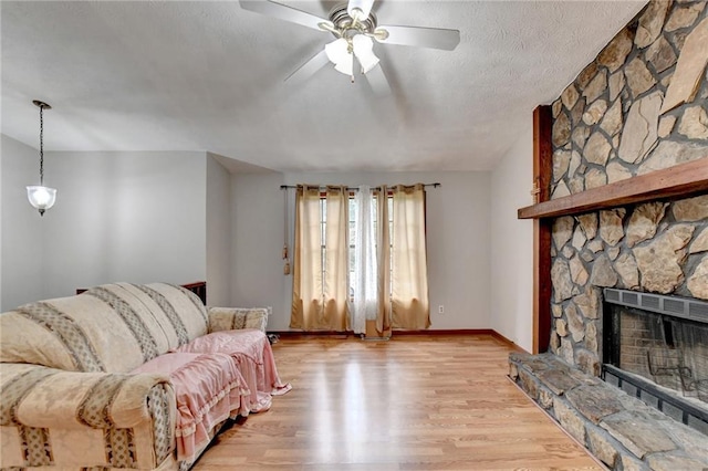 living room with ceiling fan, light hardwood / wood-style floors, a fireplace, and a textured ceiling