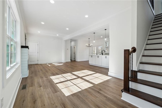 unfurnished living room featuring a notable chandelier, sink, light hardwood / wood-style floors, and a wealth of natural light