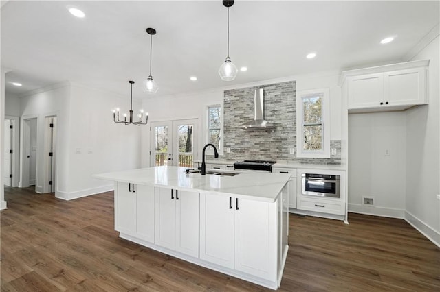 kitchen with stainless steel oven, a kitchen island with sink, sink, and wall chimney range hood