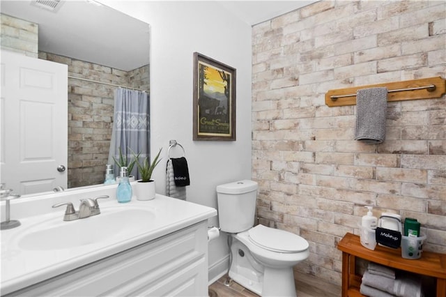 bathroom featuring vanity, wood-type flooring, toilet, and brick wall