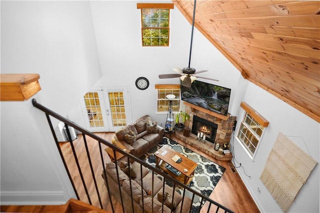 living room with ceiling fan, high vaulted ceiling, a stone fireplace, and hardwood / wood-style flooring