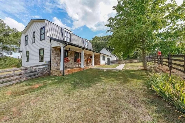 rear view of property featuring a gambrel roof, metal roof, a yard, a fenced backyard, and stone siding