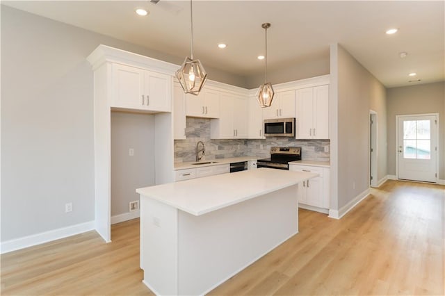 kitchen with sink, appliances with stainless steel finishes, white cabinets, a kitchen island, and decorative light fixtures