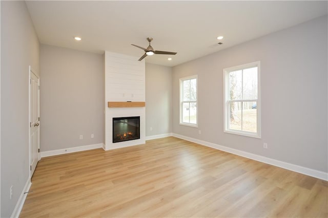 unfurnished living room featuring a large fireplace, ceiling fan, and light wood-type flooring