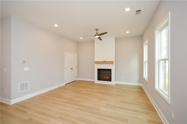 unfurnished living room with ceiling fan, a large fireplace, a healthy amount of sunlight, and light wood-type flooring