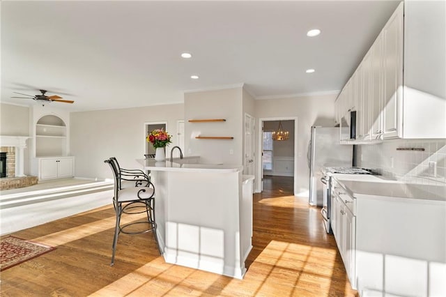 kitchen with a ceiling fan, light wood finished floors, a breakfast bar, appliances with stainless steel finishes, and white cabinetry