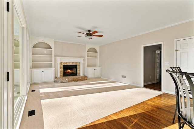 unfurnished living room featuring visible vents, built in shelves, a ceiling fan, wood finished floors, and baseboards