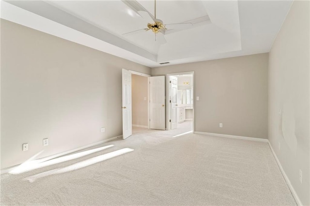 unfurnished room featuring visible vents, a ceiling fan, a tray ceiling, baseboards, and light colored carpet