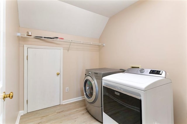 clothes washing area featuring baseboards, light wood-style floors, washing machine and dryer, and laundry area