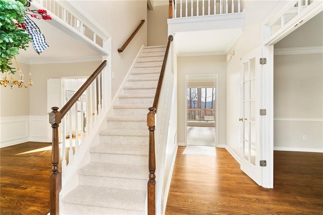 stairway with wainscoting, wood finished floors, and crown molding