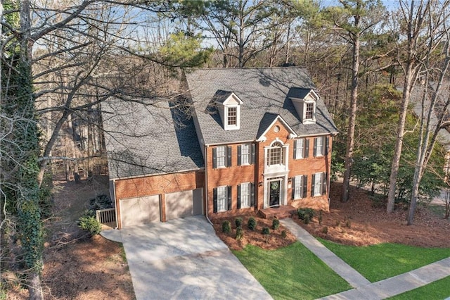 colonial-style house featuring an attached garage, brick siding, driveway, and a shingled roof