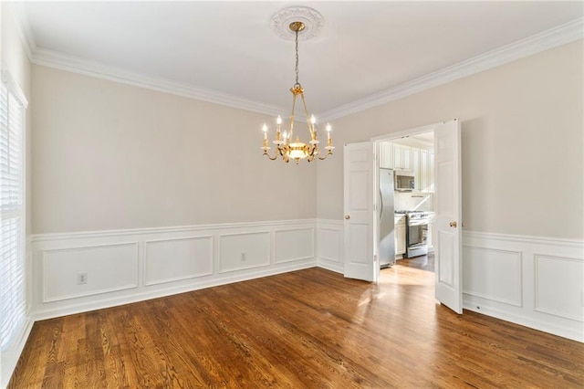 spare room with a wainscoted wall, crown molding, an inviting chandelier, and wood finished floors