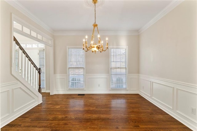 unfurnished dining area with stairway, dark wood finished floors, ornamental molding, a decorative wall, and a chandelier