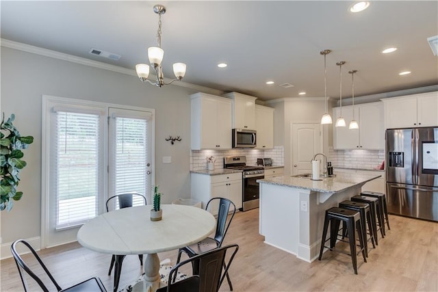 6410 Crosscreek Ln, Flowery Branch, GA 30542 - kitchen featuring appliances with stainless steel finishes, ornamental molding, a kitchen breakfast bar, backsplash, and an island with sink