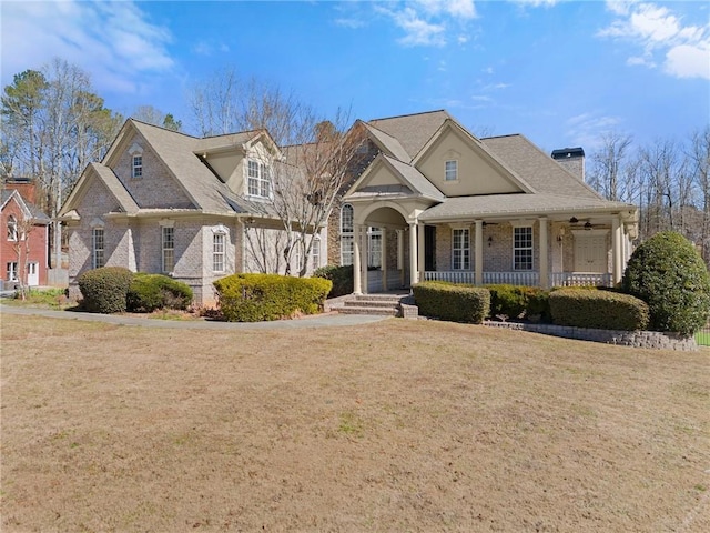 view of front of home featuring a porch, brick siding, a chimney, and a front yard