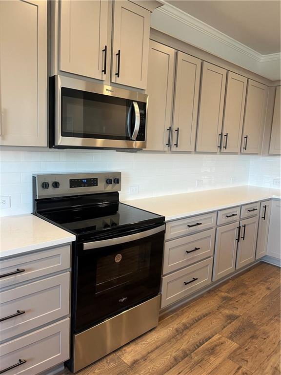 kitchen with dark wood-style flooring, ornamental molding, decorative backsplash, gray cabinetry, and appliances with stainless steel finishes