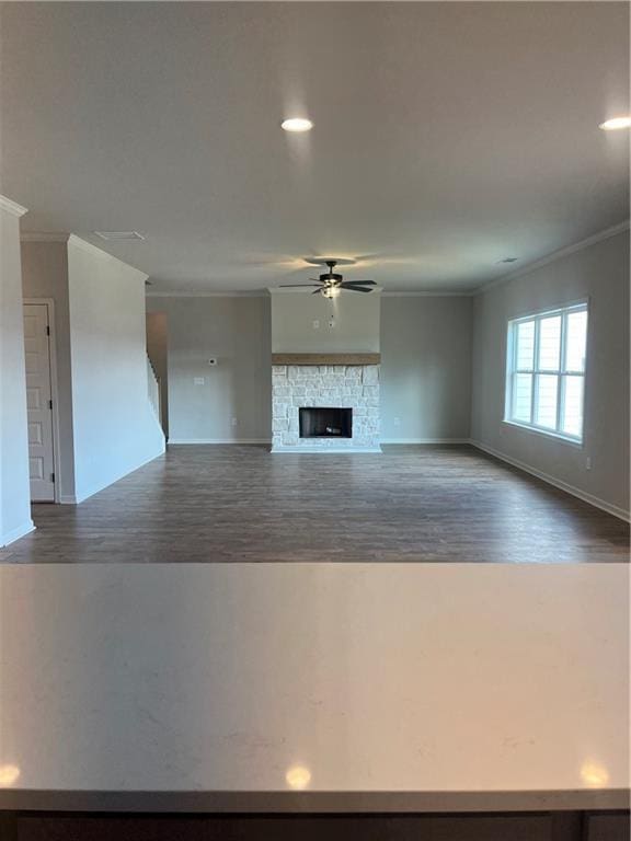 unfurnished living room with a fireplace, ceiling fan, dark wood finished floors, and crown molding