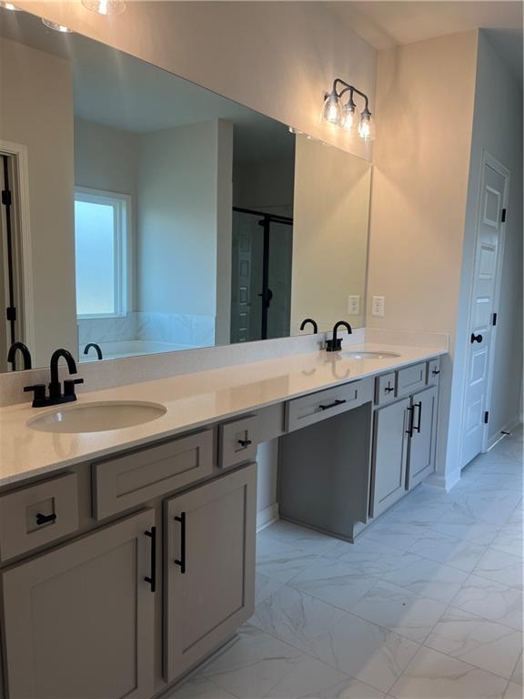 full bath featuring a sink, a shower with shower door, marble finish floor, and double vanity