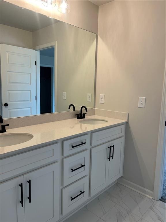 full bath with double vanity, marble finish floor, baseboards, and a sink