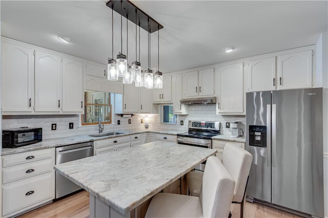 kitchen with stainless steel appliances, light hardwood / wood-style floors, a kitchen island, tasteful backsplash, and a breakfast bar