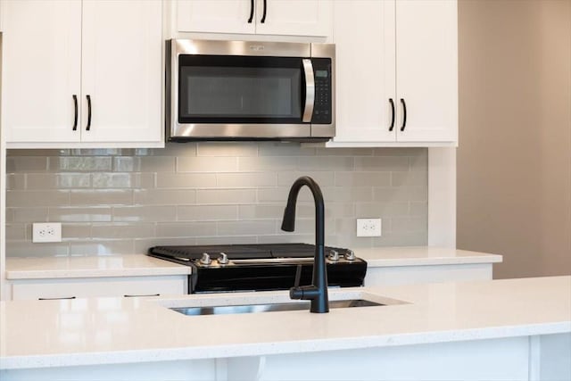 kitchen with tasteful backsplash, white cabinetry, light stone countertops, and sink