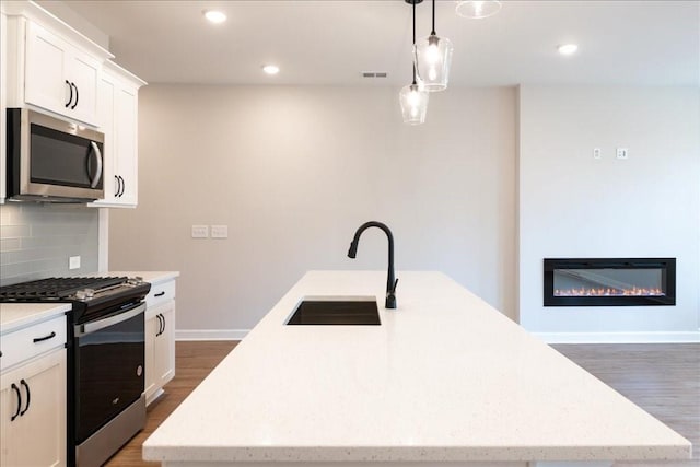 kitchen with sink, white cabinetry, decorative light fixtures, appliances with stainless steel finishes, and a kitchen island with sink