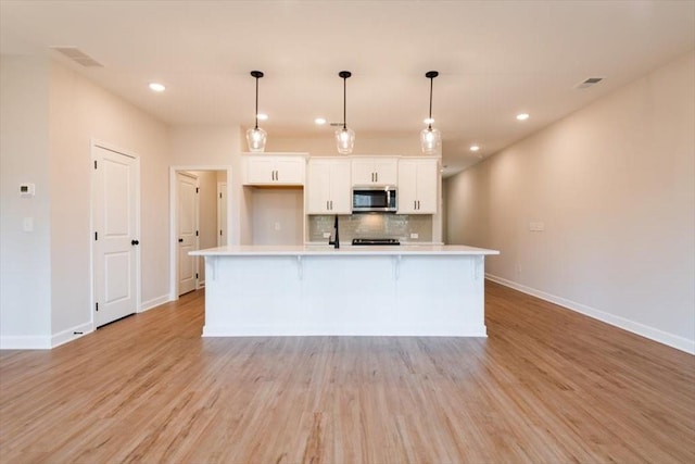 kitchen featuring pendant lighting, backsplash, an island with sink, white cabinets, and light wood-type flooring