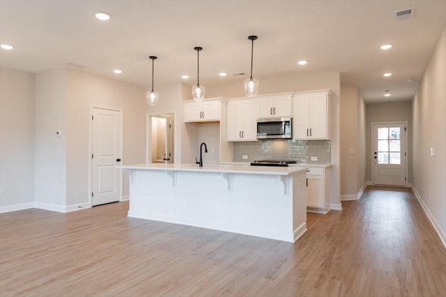 kitchen with white cabinetry, a breakfast bar area, hanging light fixtures, a kitchen island with sink, and light hardwood / wood-style flooring