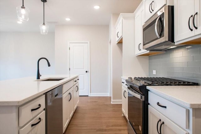 kitchen with sink, appliances with stainless steel finishes, hanging light fixtures, white cabinets, and a center island with sink