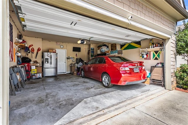 garage featuring stainless steel fridge with ice dispenser, a garage door opener, and driveway