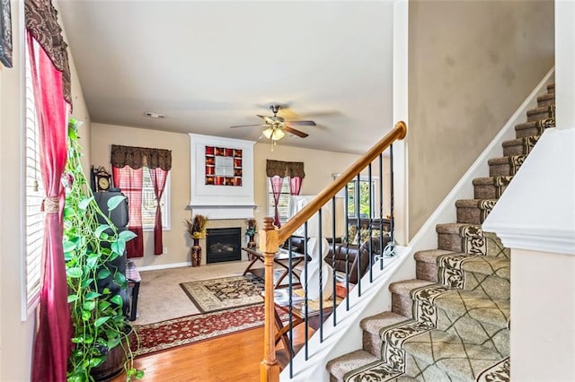 stairway featuring a glass covered fireplace, ceiling fan, and visible vents