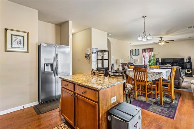 kitchen featuring light stone countertops, ceiling fan with notable chandelier, open floor plan, stainless steel fridge, and dark wood-type flooring