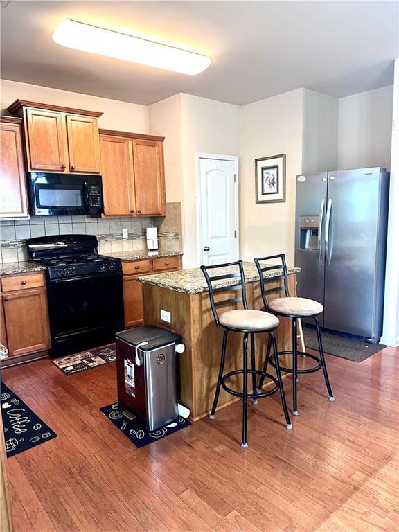 kitchen featuring a breakfast bar, wood finished floors, backsplash, a kitchen island, and black appliances