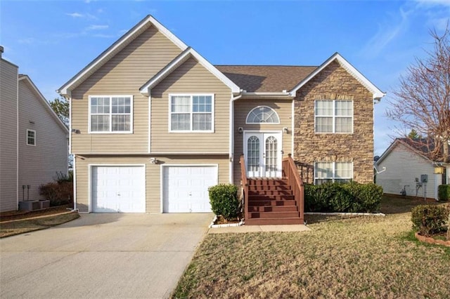 raised ranch featuring a garage, a front yard, and central air condition unit