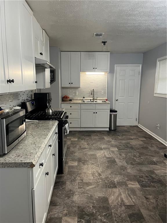 kitchen featuring appliances with stainless steel finishes, white cabinetry, tasteful backsplash, a textured ceiling, and sink