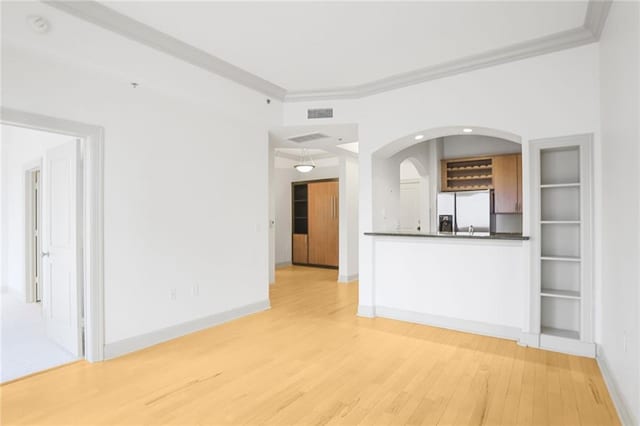 unfurnished living room with light wood-type flooring, baseboards, and crown molding