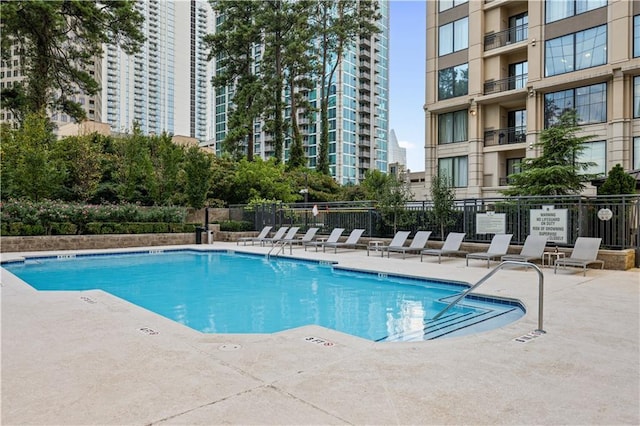 community pool with a patio area, fence, and a city view