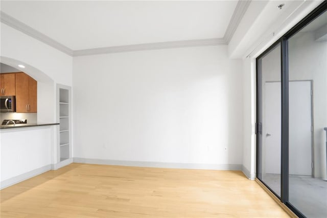 interior space with arched walkways, crown molding, stainless steel microwave, brown cabinetry, and light wood-style floors