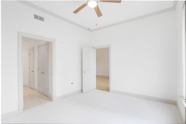 empty room with baseboards, visible vents, a ceiling fan, light colored carpet, and crown molding