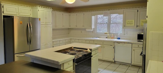 kitchen with sink, dishwasher, tile counters, stainless steel refrigerator, and black range with electric cooktop