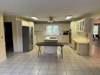 kitchen featuring a kitchen breakfast bar, ceiling fan, light tile patterned floors, stainless steel refrigerator, and a kitchen island