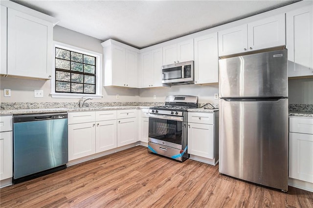 kitchen with sink, stainless steel appliances, light stone counters, light hardwood / wood-style flooring, and white cabinets